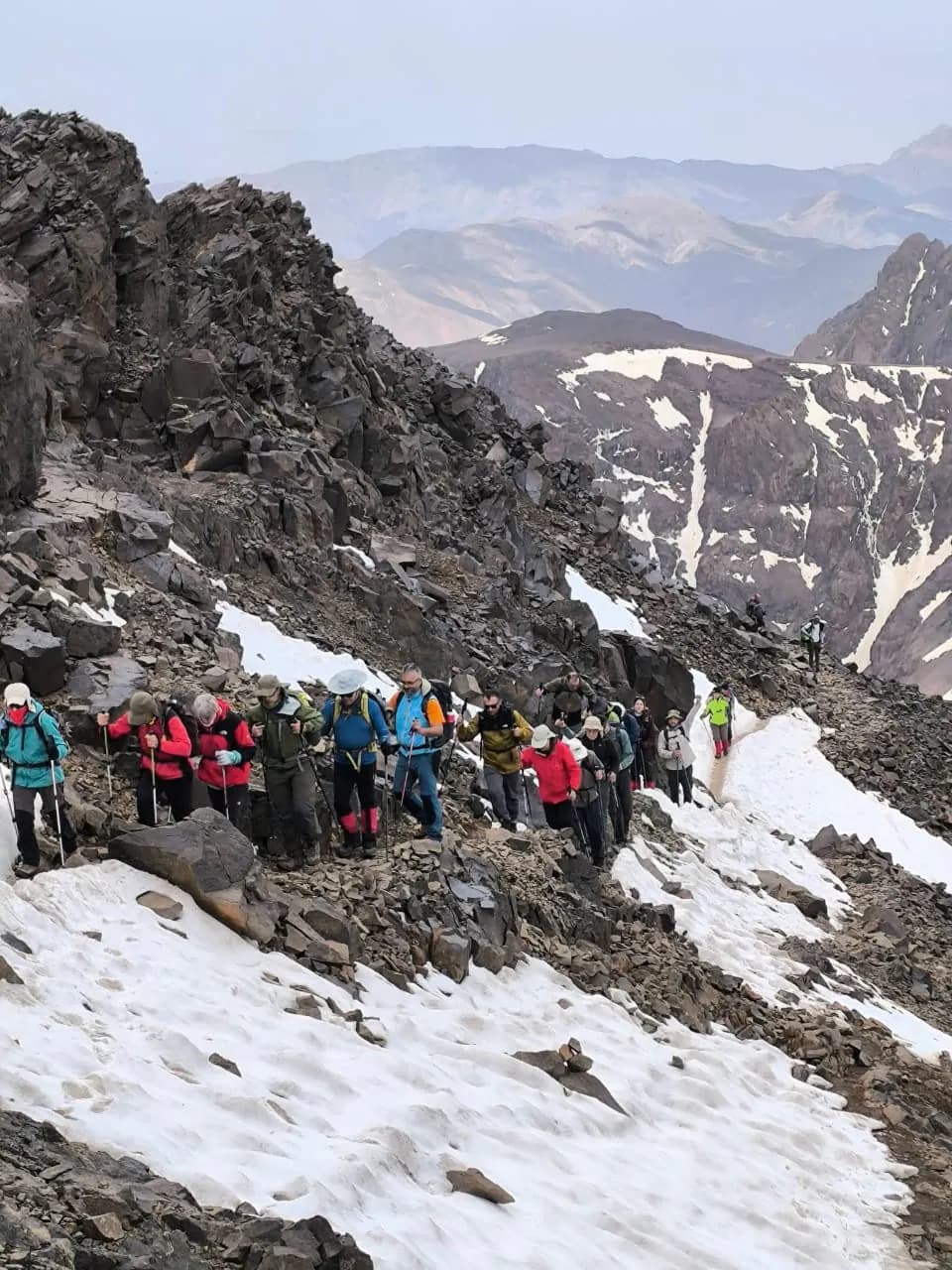 A group of trekkers on a rocky slope patched with snow