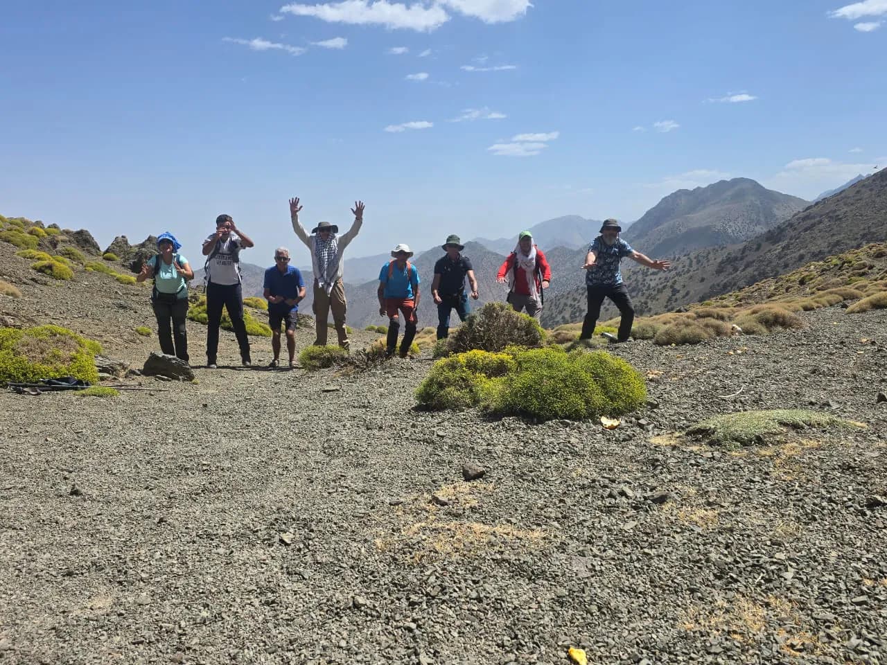 Un groupe de randonneurs, certains les bras levés, sur un plateau caillouteux sous un ciel bleu