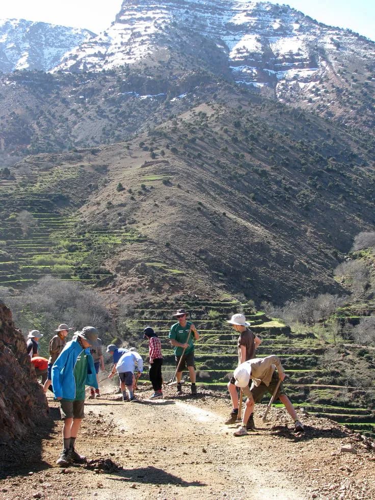 Un groupe de personnes sur un chemin de terre, devant des versants en terrasses et des montagnes enneigées